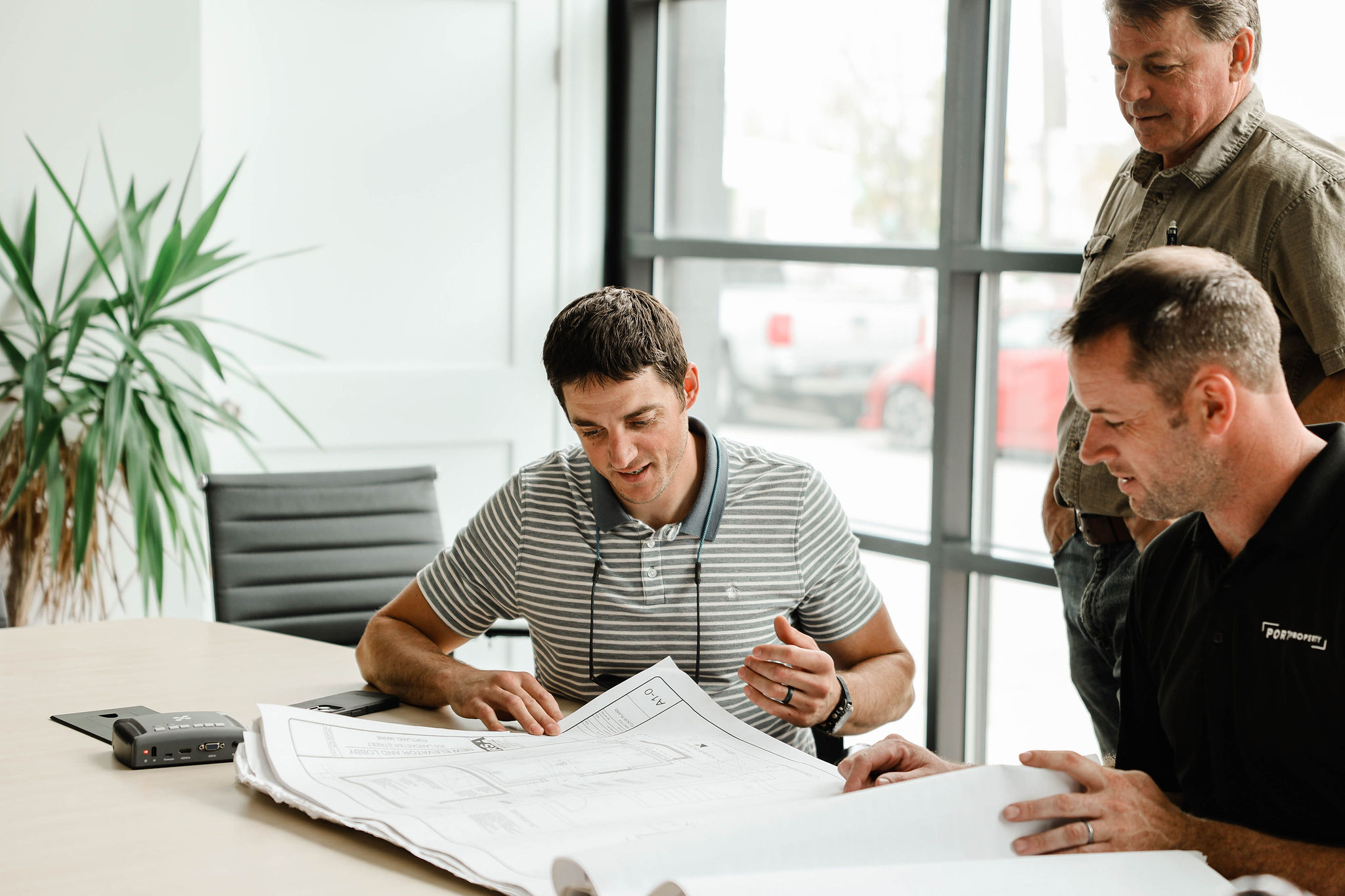 Photo of a group of three men sitting around a table discussing building plans.