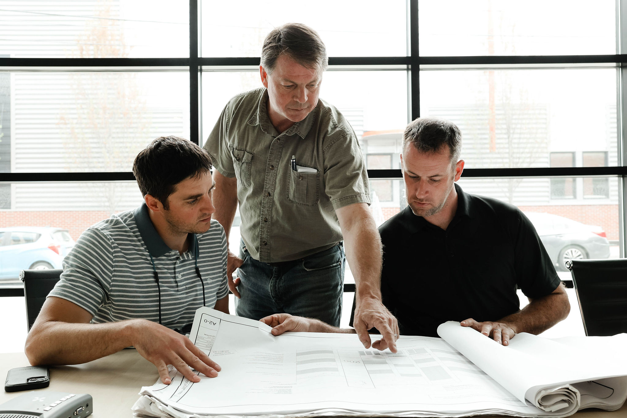 Photo of a group of three men sitting around a table discussing building plans.