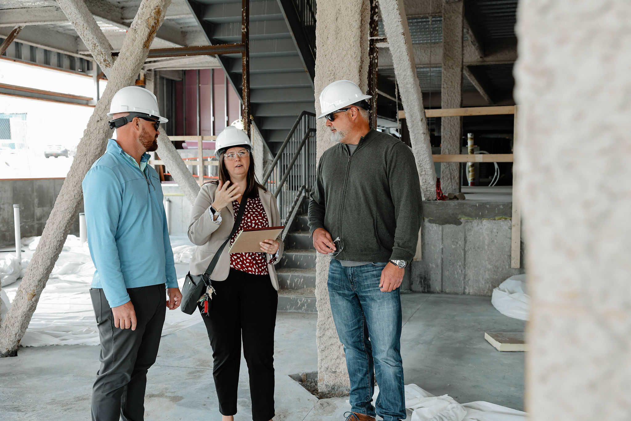 A photograph of three people at a construction site, wearing hardhats, discussing plans.